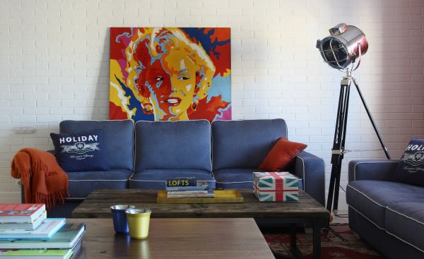 客厅摆放着蓝色的沙发，以及沙发的背景墙放置着炫彩的画，点缀着整个客厅的艺术气息